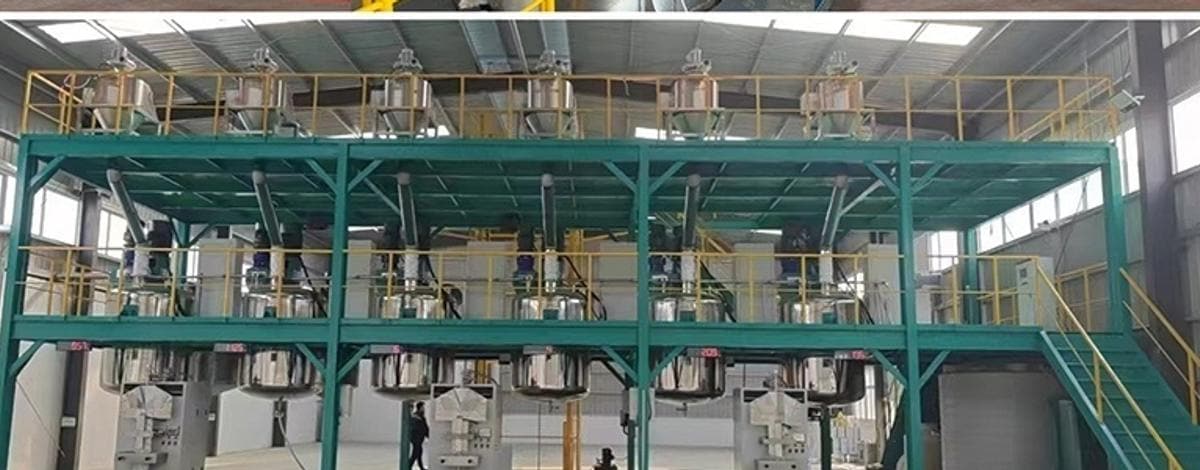 Vista geral da oficina parceira: fileiras de cubas de emulsificação e dispersão sobre uma plataforma de aço, com moinhos de contas no piso abaixo